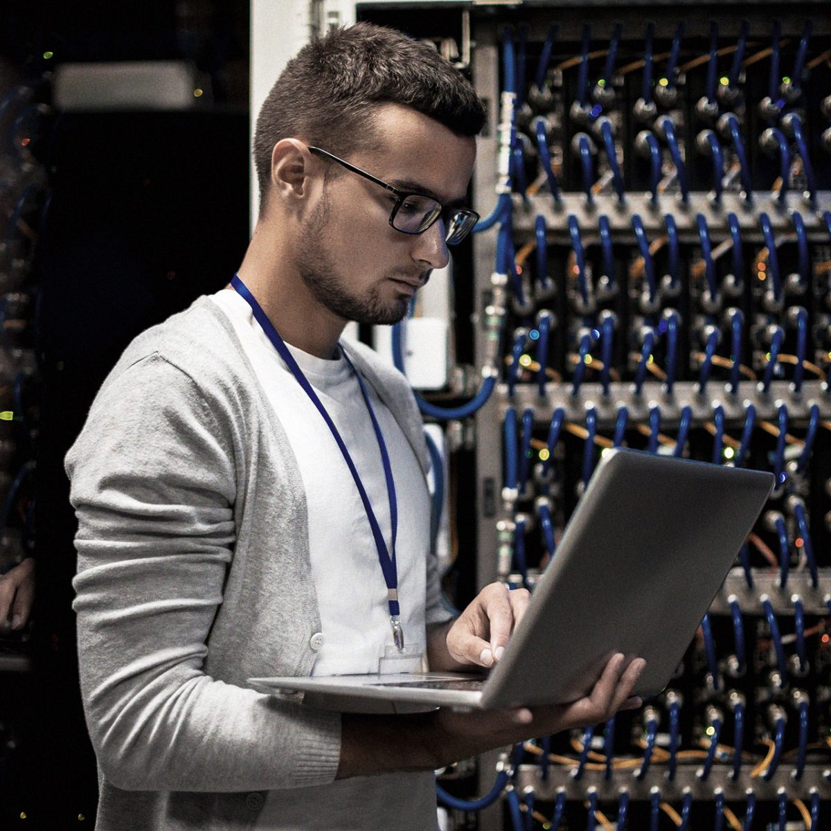 Side view portrait of young man with laptop standing by server cabinet while working with supercomputer